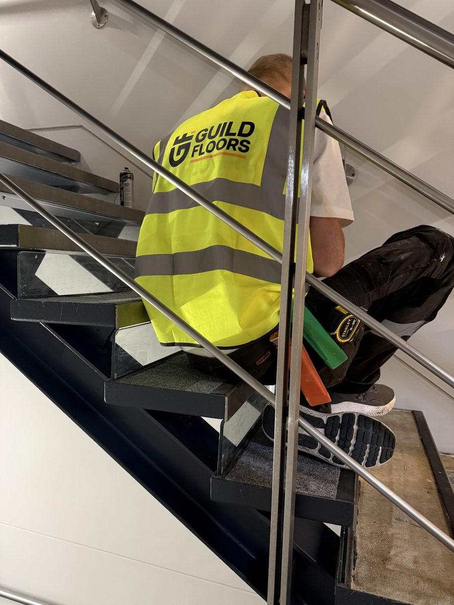 A Guild Floors fitter in a branded hi-vis vest working on a commercial staircase
